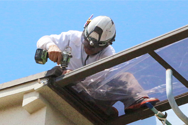 カーポート屋根の接合部をビスで固定、補修工事を行う職人